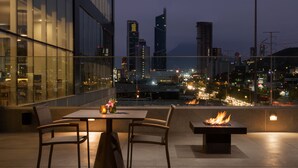 A rooftop terrace with a table and chairs, a fire feature, and a cityscape view at dusk. - Hyatt House Monterrey Valle-san Pedro (San Pedro Garza García)
