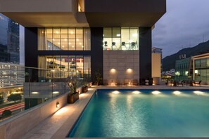 A modern building with a swimming pool, glass railings, and outdoor seating.