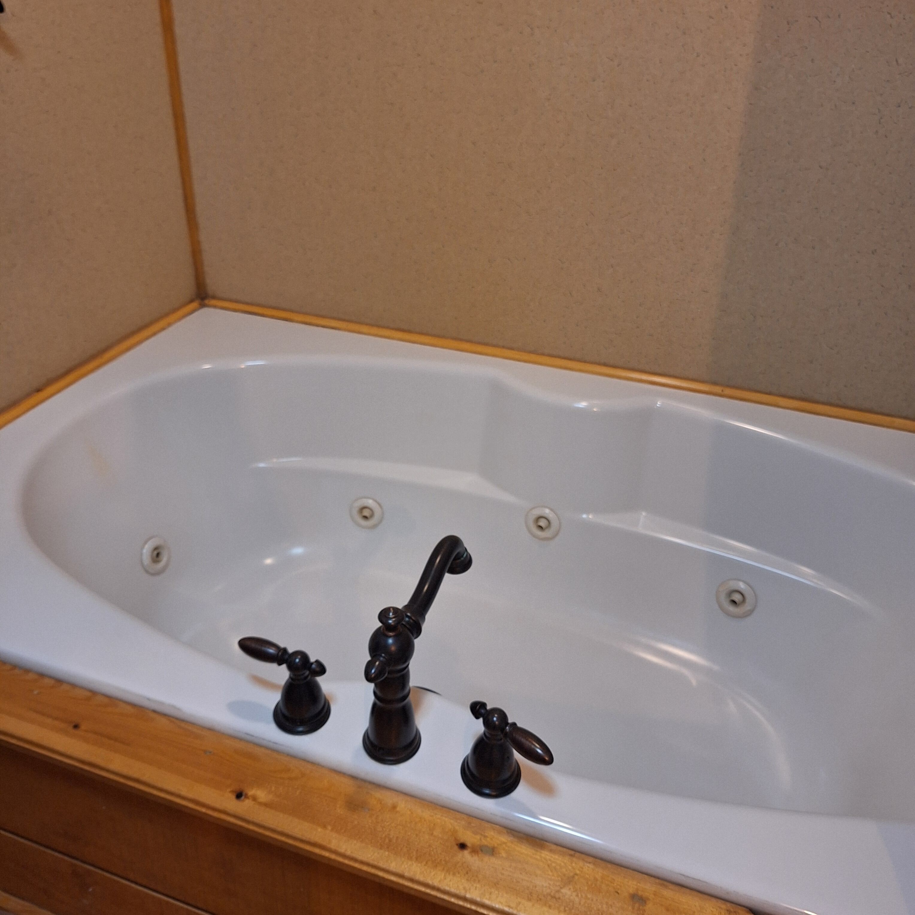 A white bathtub with three black faucets and wooden trim.