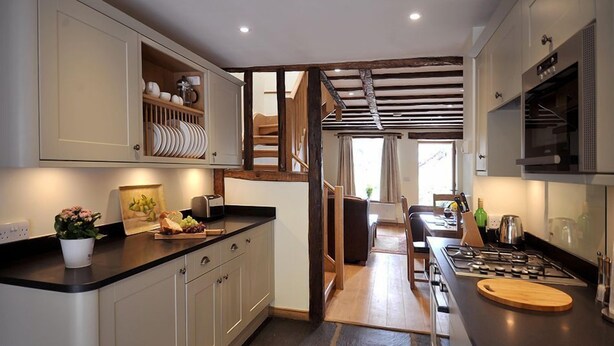 A modern kitchen with a central island, built-in cabinets, and a staircase leading to an upper level. - No. 2 The Forge, village cottage in idyllic riverside setting (Coniston)