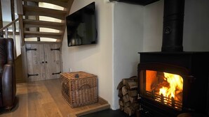 A cozy room with a fireplace, a television mounted on the wall, and a wooden door. - No. 2 The Forge, village cottage in idyllic riverside setting (Coniston)