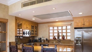 A kitchen with wooden cabinets, a stainless steel refrigerator, and a bar area with chairs. - Located on the pristine medano beach (Cabo San Lucas)