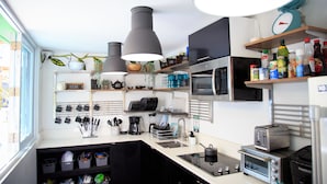 Una cocina moderna con microondas, tostadora y diversos electrodomésticos. Hay estantes con utensilios de cocina y una ventana con vistas al exterior.