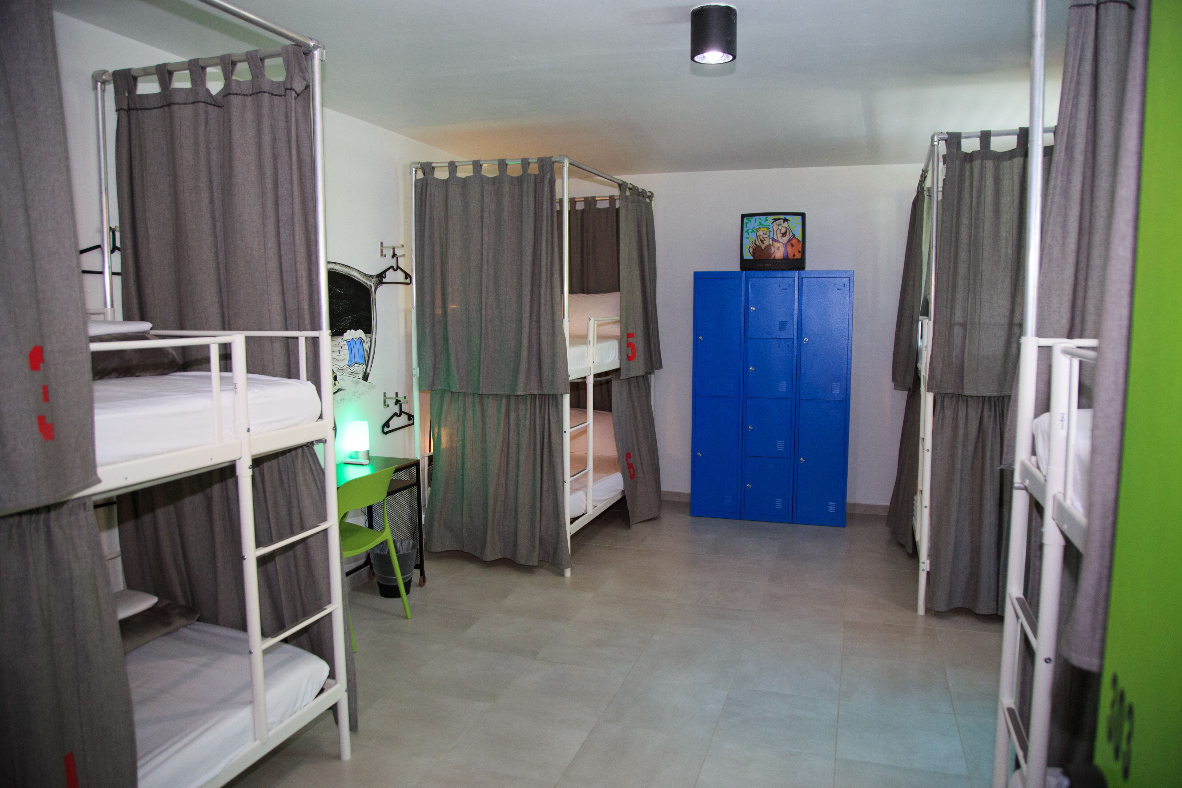 A dormitory room with bunk beds, a desk with a lamp, and blue lockers.