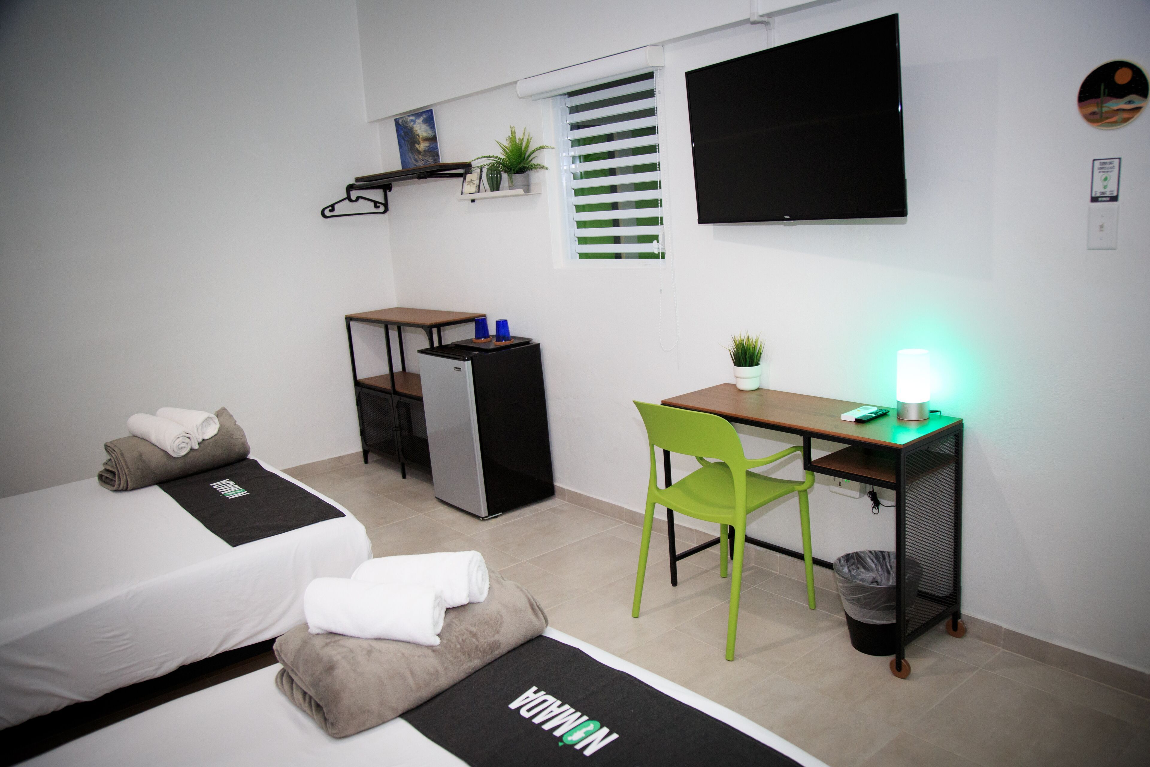 Una habitación de hotel compacta con cama, escritorio, silla, kitchenette pequeña y televisor.