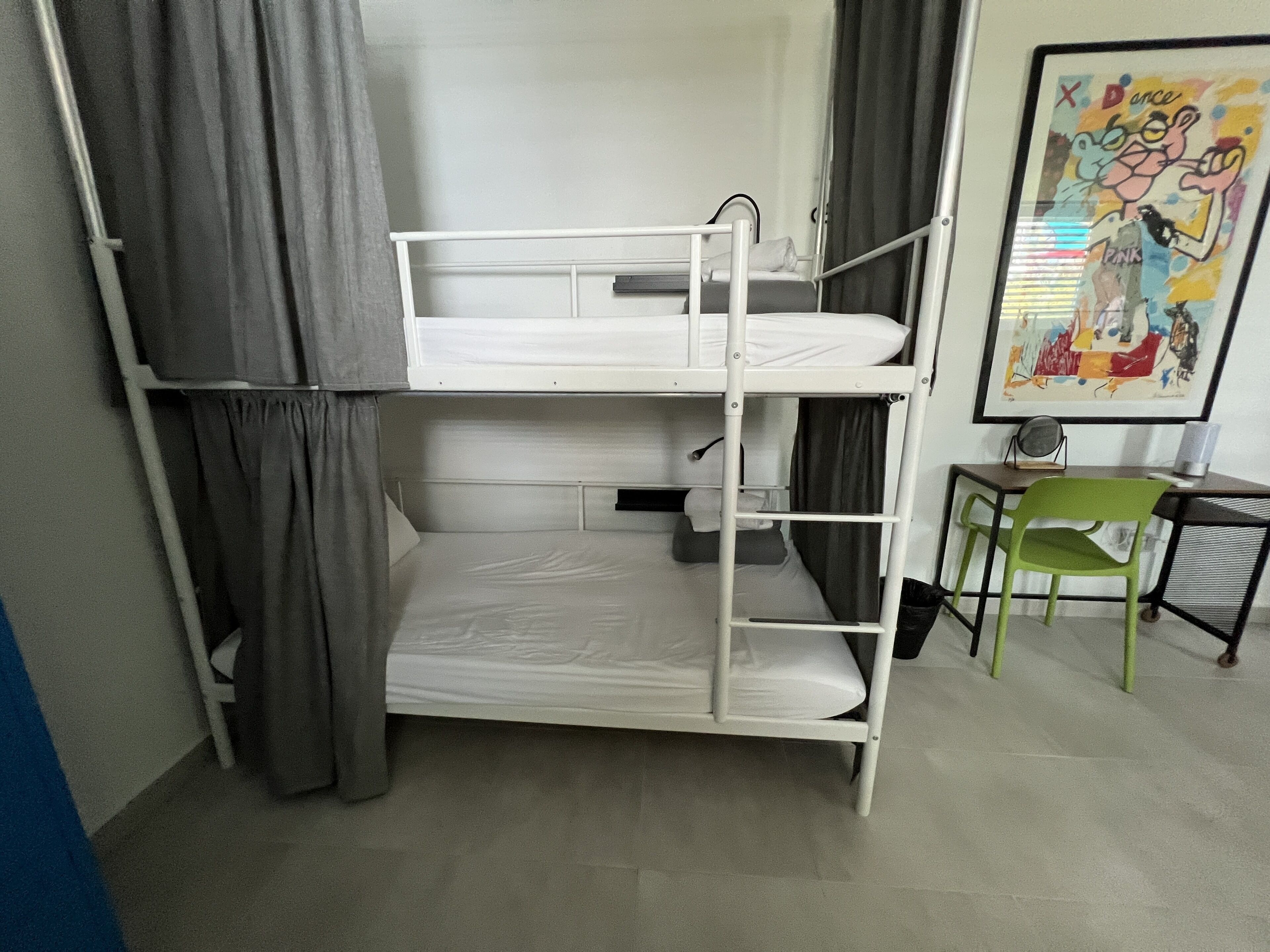 A bunk bed with a desk and chair, a framed picture on the wall, and a curtain.