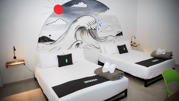 Habitación de hotel con dos camas, un mural de una ola y un sol rojo.