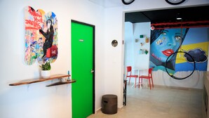 Un pasillo con una puerta verde, un muro con un mural colorido y una silla roja al fondo.