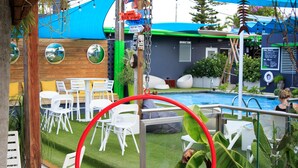 Un área de estar al aire libre con sillas y mesas blancas, una piscina y una pérgola de madera.