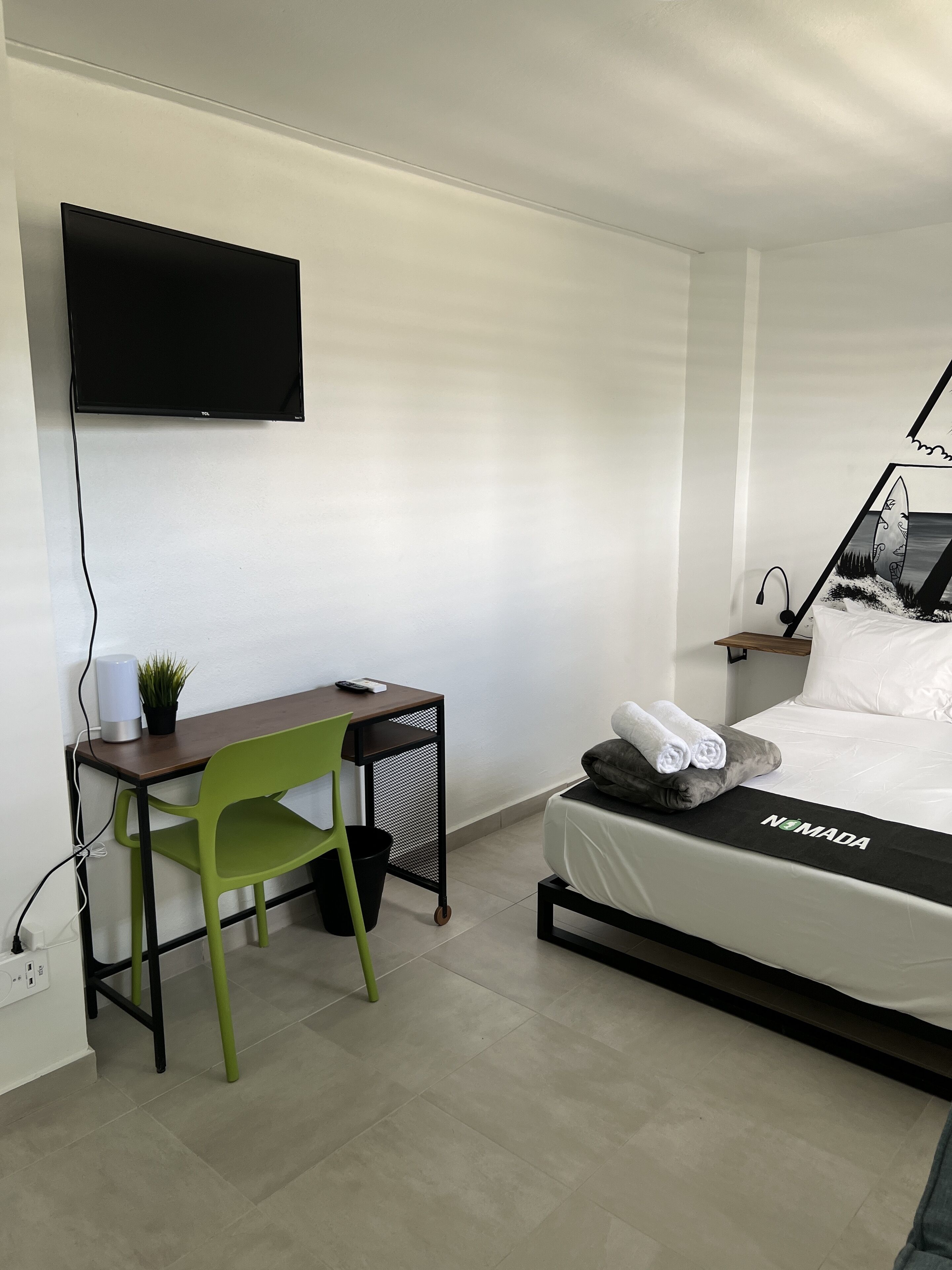 A modern hotel room with a bed, a desk, a chair, a TV, and a wall-mounted artwork.
