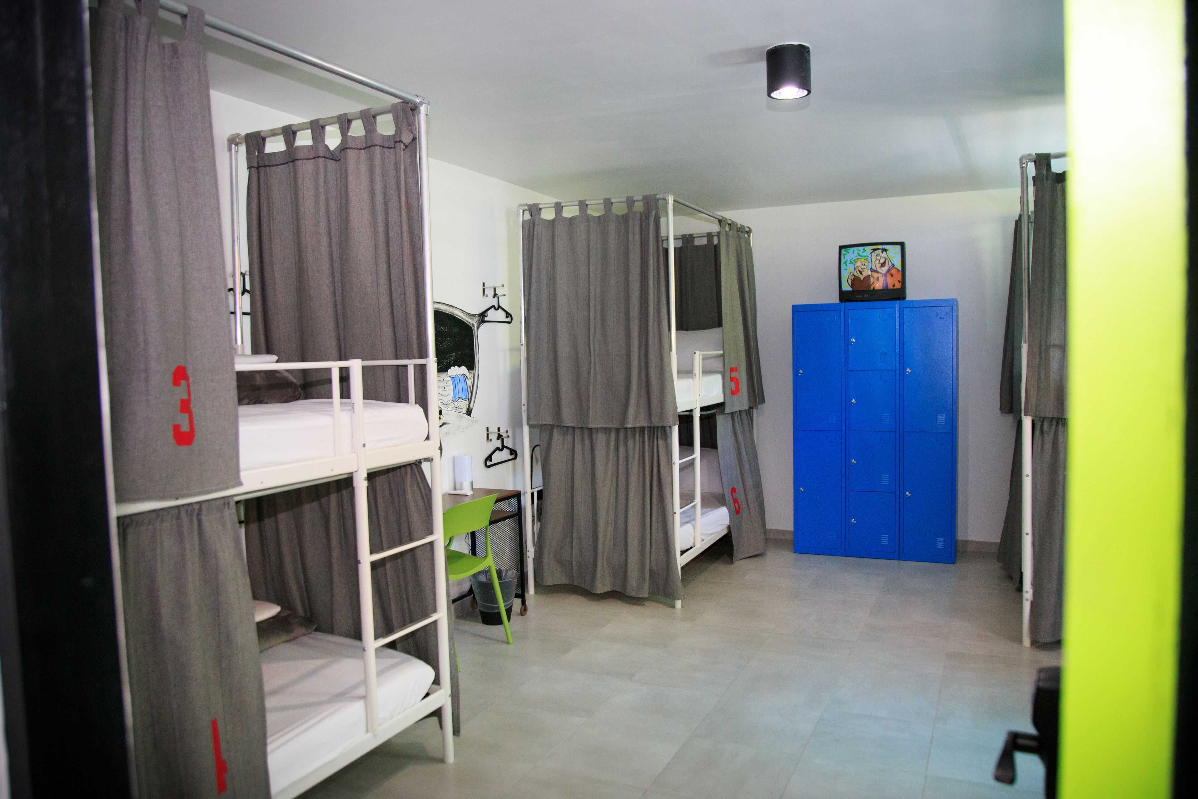 Ein Schlafsaalzimmer mit Etagenbetten, einem Schreibtisch, einem Stuhl und einem blauen Kleiderschrank.
