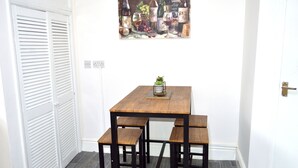 A dining area with a wooden table and benches, a painting above the table, and a white door with louvered shutters. - Beautiful Two-bed Apartment With Driveway Parking (Nottingham)