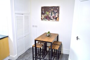 A small dining area with a wooden table and four stools, a wall-mounted painting of wine bottles, and a white door with a handle. - Beautiful Two-bed Apartment With Driveway Parking (Nottingham)