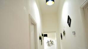 A narrow hallway with white walls, a ceiling light, a door at the end, and a circular wall decoration. - Beautiful Two-bed Apartment With Driveway Parking (Nottingham)