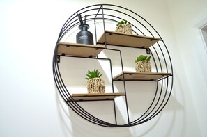 A wall-mounted circular shelf unit with three shelves, each holding a small potted plant and a black bottle labeled "UNWIND". - Beautiful Two-bed Apartment With Driveway Parking (Nottingham)