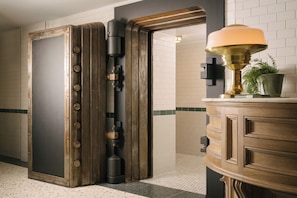 A hotel lobby with a large safe, a wooden cabinet with a lamp, and a potted plant.