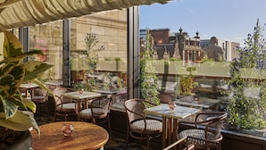 An outdoor seating area with wicker chairs and tables, large windows with a view of buildings, and potted plants. - Gleneagles Townhouse (Edinburgh)