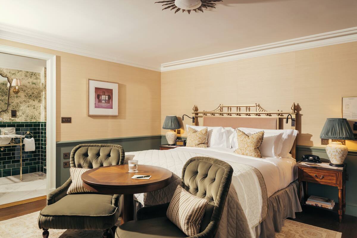 A hotel room with a bed, two bedside tables, a round table, two chairs, a mirror, and a framed picture on the wall.