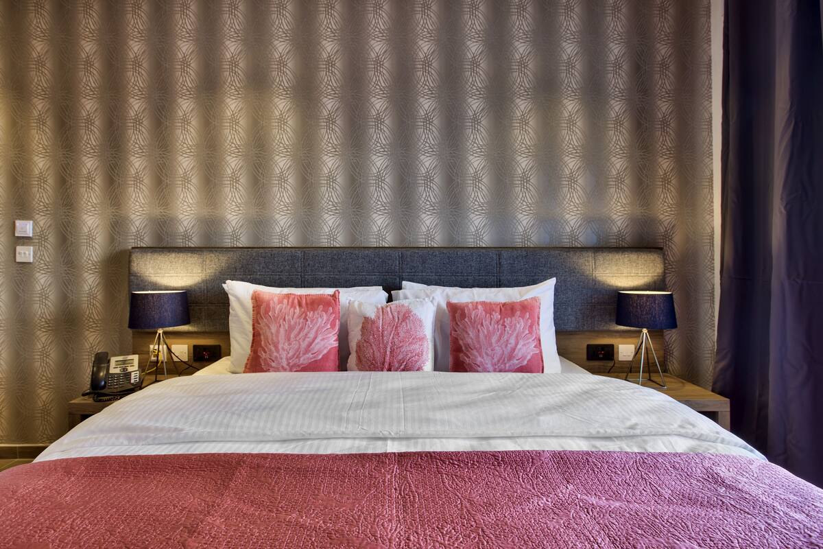 Une chambre d’hôtel avec un grand lit, deux lampes de chevet, un téléphone et un rideau à motifs.