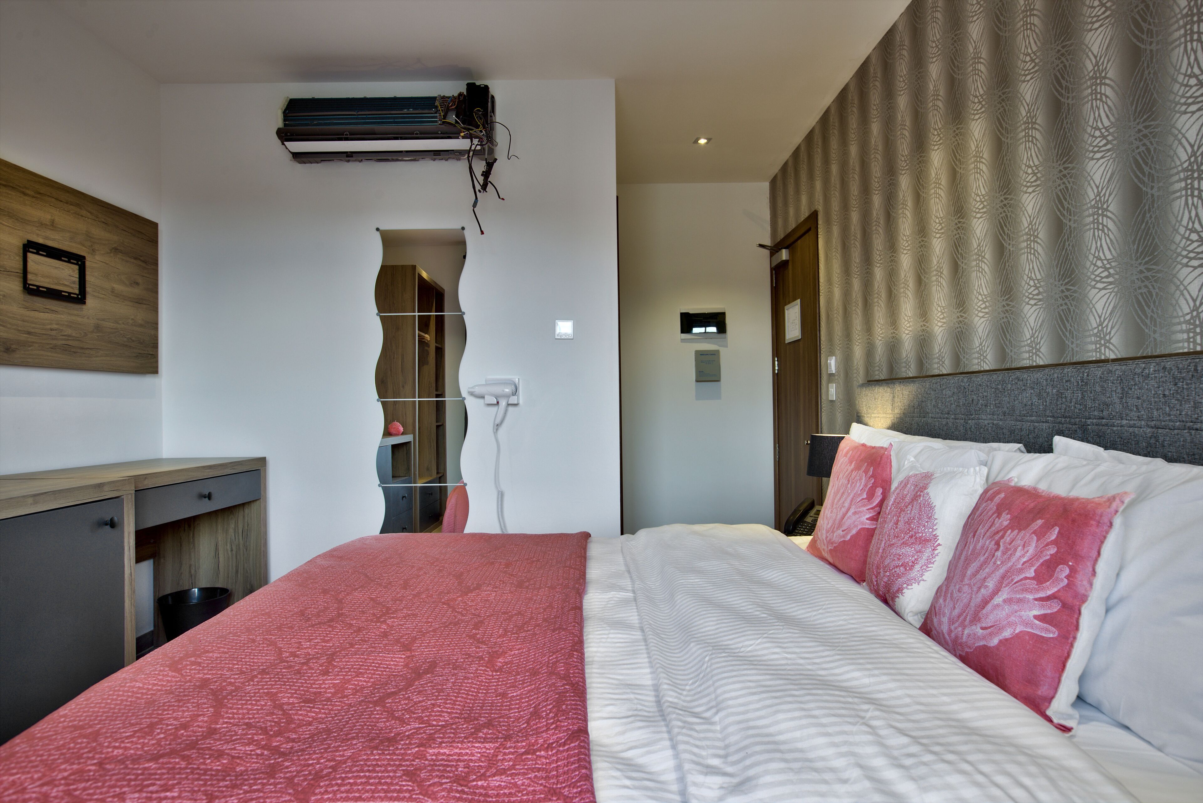A modern hotel room with a large bed, a wooden desk, and a unique wall design.