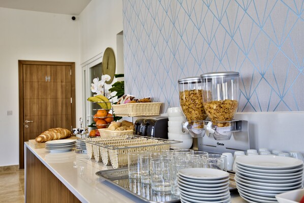 A buffet setup with various food items, a coffee machine, and stacked plates and glasses. - Tritoni Valletta Boutique Hotel (Floriana)