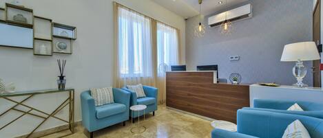 A modern hotel lobby with a reception desk, blue sofas, a small round table, and a decorative lamp.