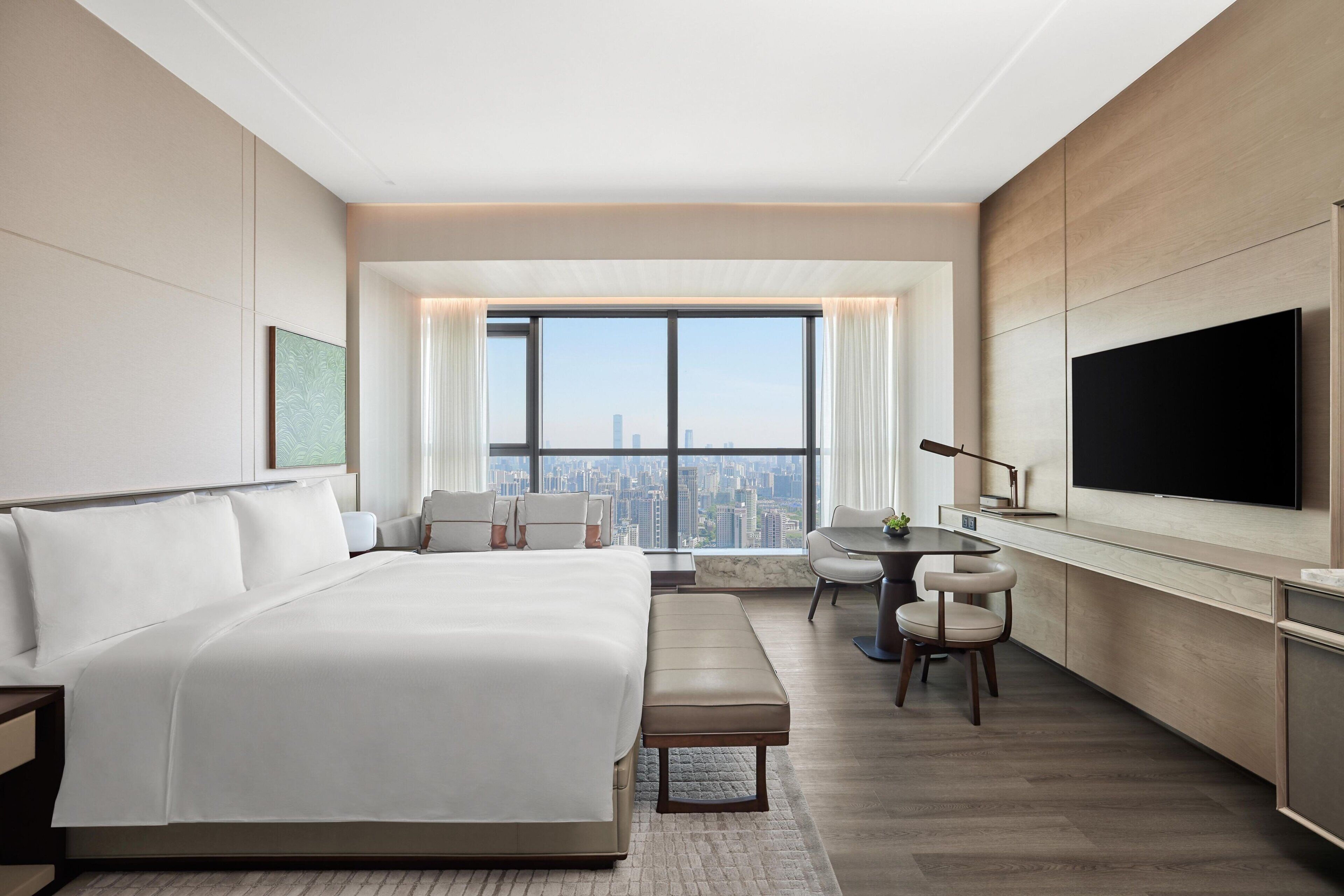 A modern hotel room with a large bed, a desk, a chair, and a TV.