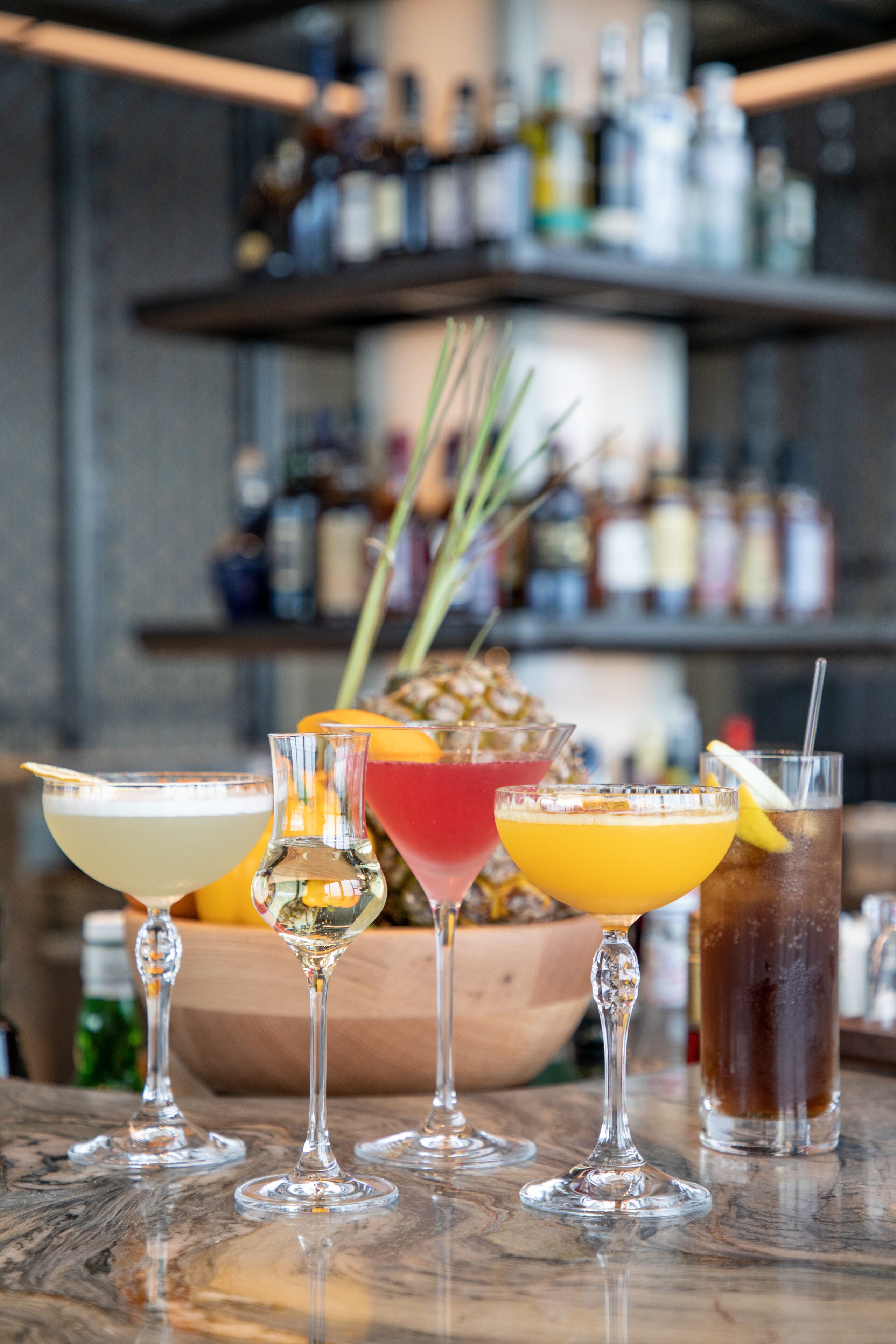 Un bar con diversas bebidas en vasos, una piña y una botella de licor en estantes.