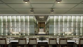 A modern restaurant with a long counter, cushioned seating, and a central walkway.