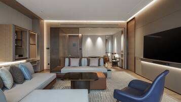 A modern hotel room with a sofa, a coffee table, a TV, and a seating area with a chair.