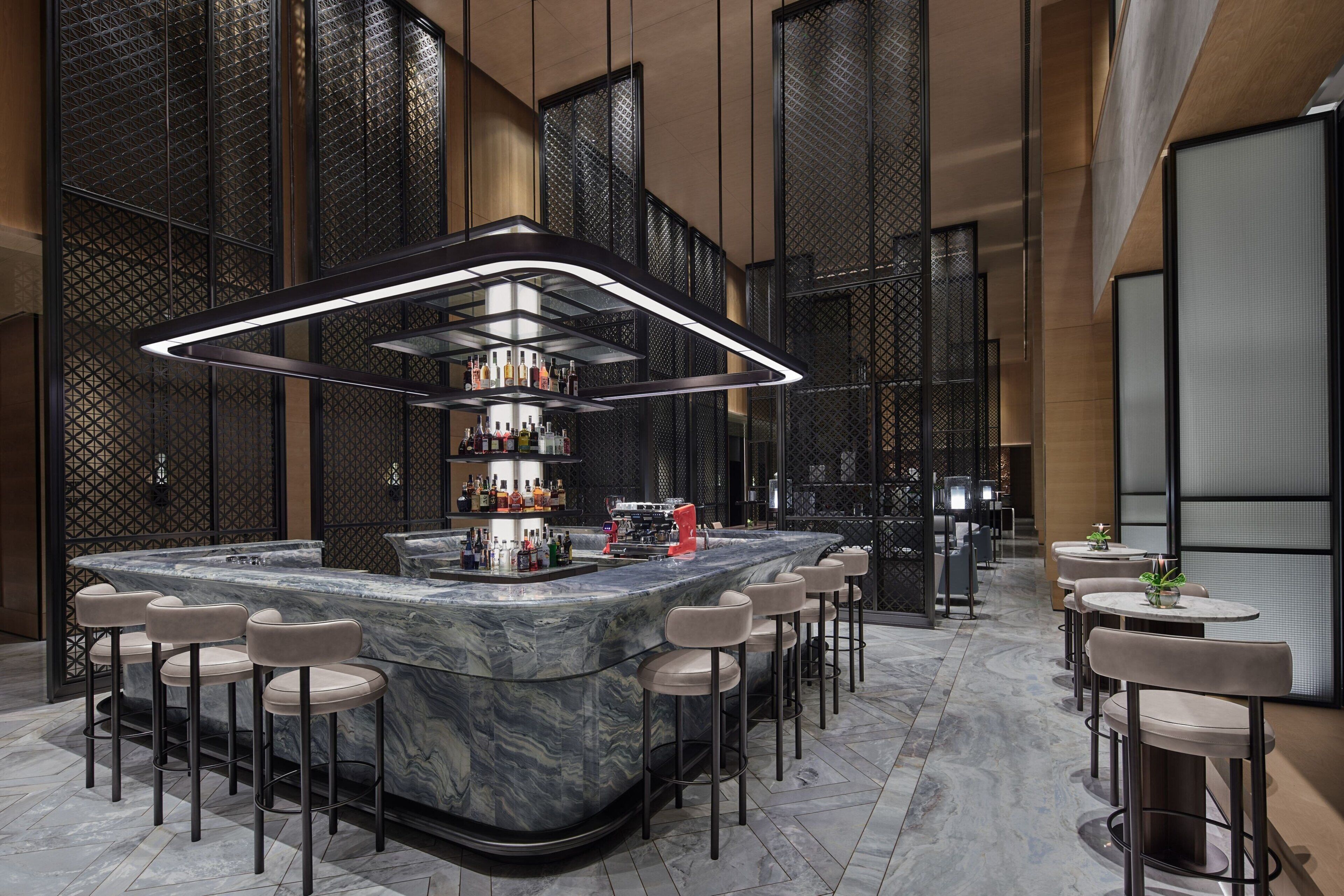 A modern bar area with a marble counter, multiple stools, and a well-lit overhead light fixture.