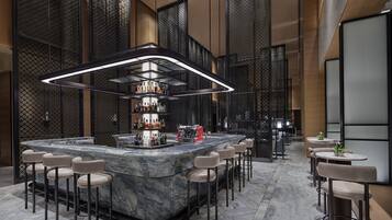 A modern bar area with a marble counter, multiple stools, and a well-lit overhead light fixture.