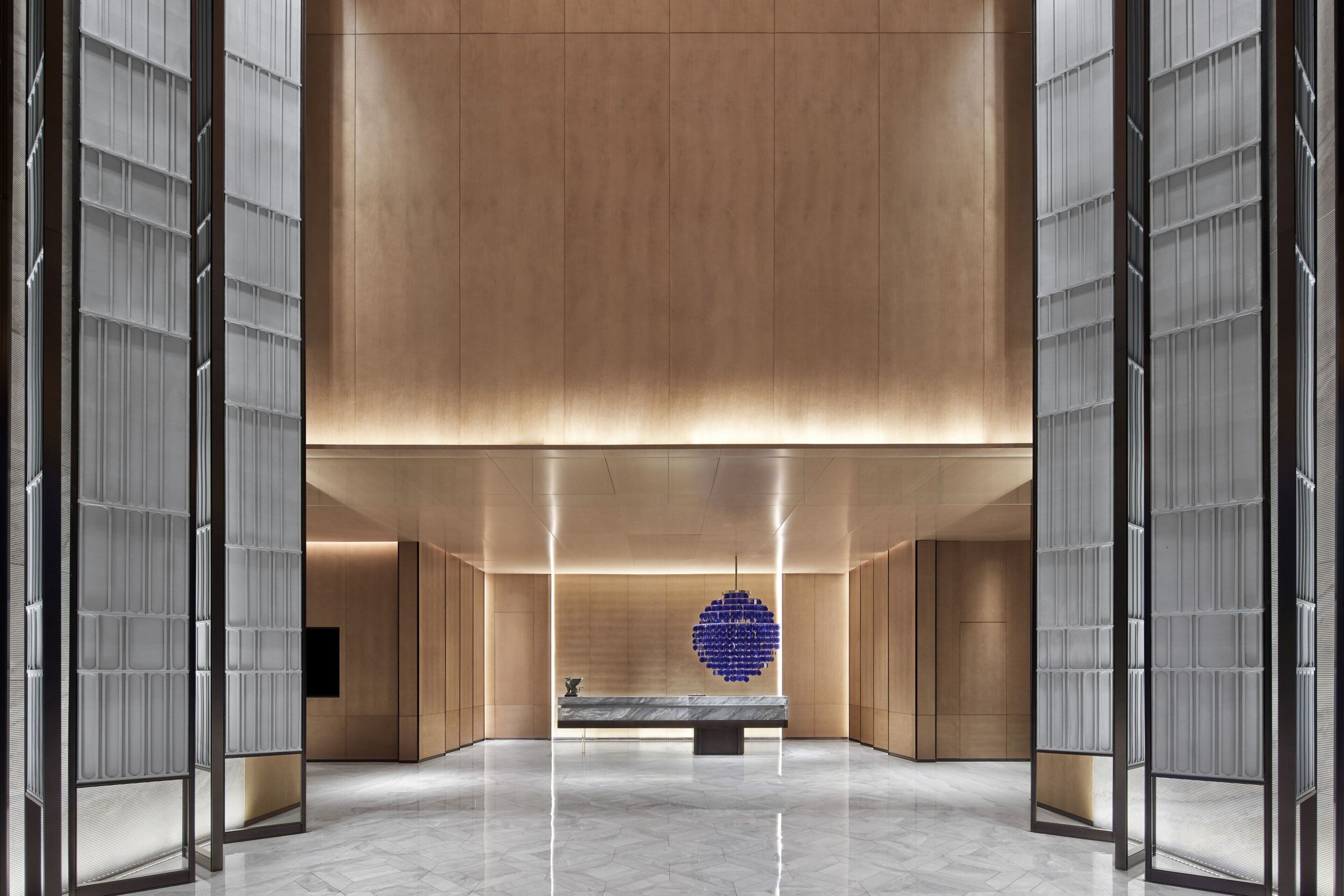 A spacious lobby with a marble floor, a reception desk, and a large blue spherical sculpture.