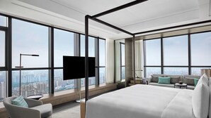 Una habitación de hotel moderna con una cama grande, televisión, sofá y vistas a la ciudad.