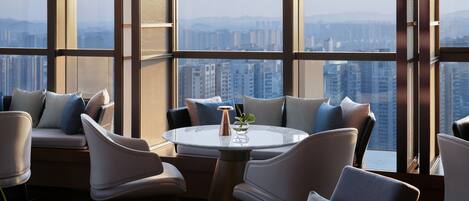 A modern interior with a round table and chairs, large windows offering a city view.