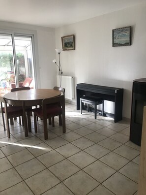 Un coin repas avec une table ronde et des chaises, un radiateur, un piano et un tableau encadré au mur.