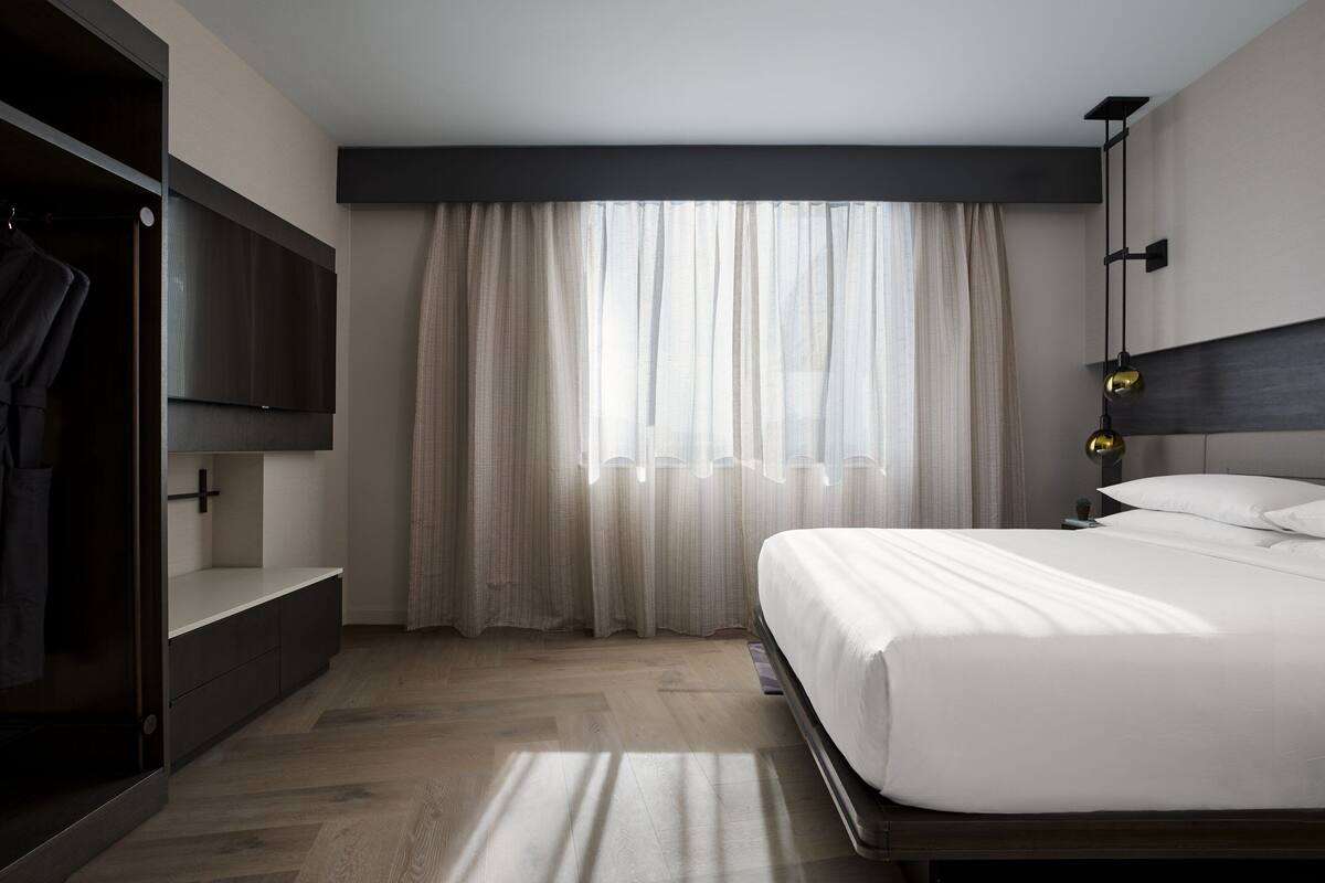 A modern hotel room with a large bed, a wardrobe, and a TV mounted on the wall.