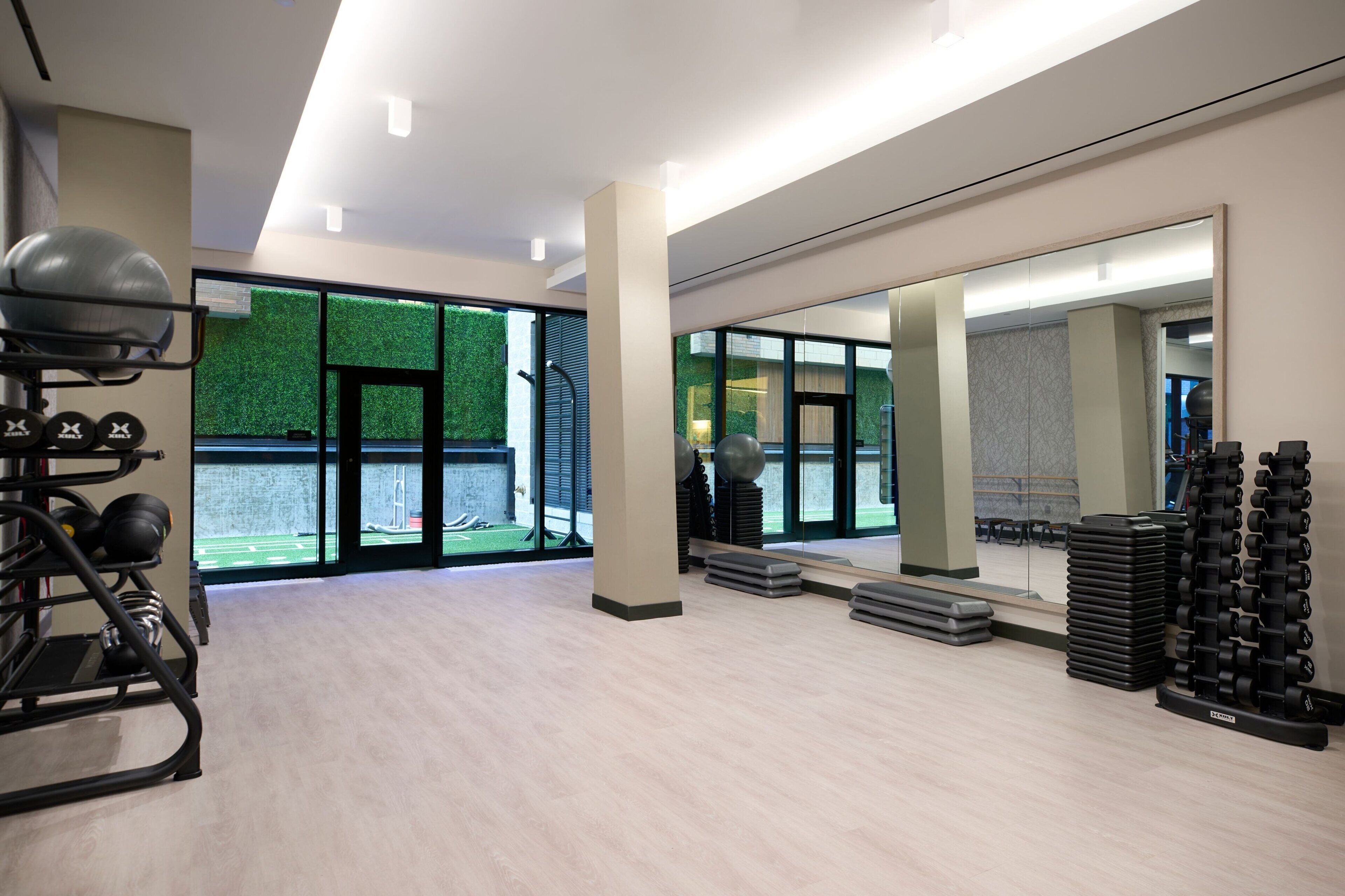 Ein modernes Fitnessstudio mit Trainingsgeräten, großen Fenstern und einer grünen Wand.