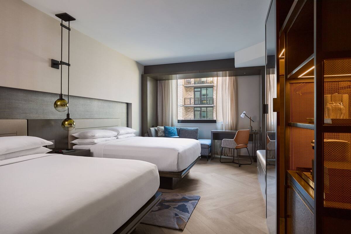 A hotel room with two beds, a desk, a chair, and a window with curtains.