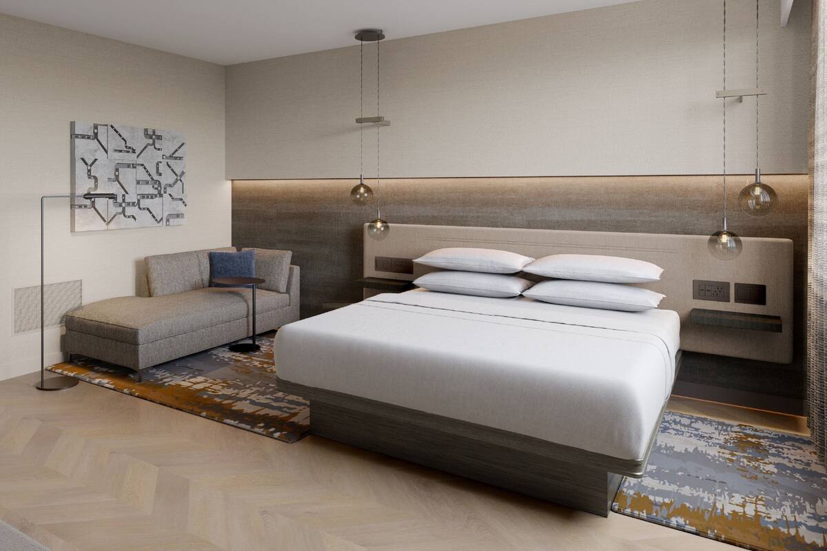 A modern bedroom with a large bed, a sofa, a floor lamp, and a wall-mounted light fixture.