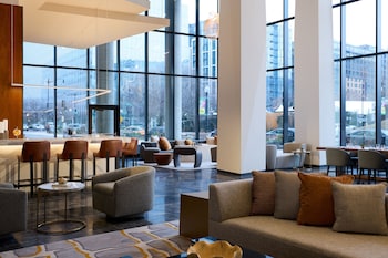A modern bar area with a long counter, bar stools, and a variety of liquor bottles. There is a seating area with sofas and chairs, and a staircase leading to another level. at Washington Marriott Capitol Hill
