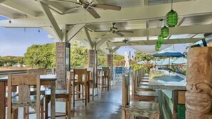 Un espace de restauration en plein air avec des tables et des chaises en bois, des ventilateurs de plafond et des lanternes suspendues.
