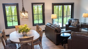 A dining area with a round table, chairs, and a potted plant. There is a sofa and a small table with a lamp in the background. - 𝗨𝗻𝗶𝗾𝘂𝗲 𝗦𝘁𝗮𝘆 at the Carriage Haus (Manitowoc)