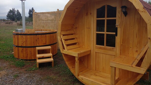A wooden cabin with a large circular window and a door, a small wooden bench, and a cylindrical structure with a chimney. - Parcela con tranque, sala de juegos, terraza, (Santa Cruz)