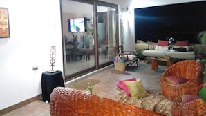 A living room with a large TV, wicker furniture, and a sliding glass door leading to another room. - Parcela con tranque, sala de juegos, terraza, (Santa Cruz)