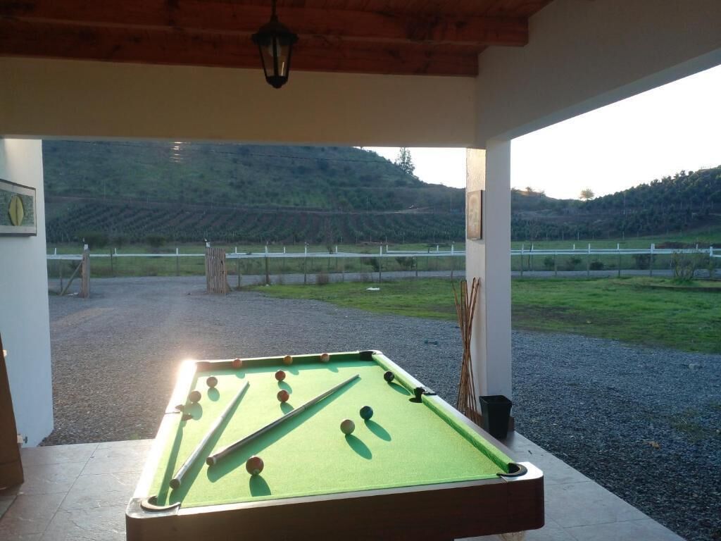 A pool table in a covered outdoor area with a view of a vineyard and hills in the background.