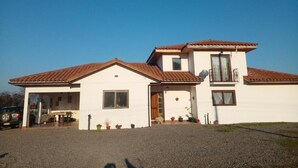 A two-story house with a tiled roof, a covered patio, and a gravel driveway. - Parcela con tranque, sala de juegos, terraza, (Santa Cruz)