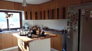 A modern kitchen with wooden cabinets, a stainless steel refrigerator, and a central island with various kitchen items. - Parcela con tranque, sala de juegos, terraza, (Santa Cruz)