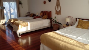 A hotel room with two beds, wooden flooring, a ceiling fan, a wall-mounted macrame decoration, and a window with curtains. - Parcela con tranque, sala de juegos, terraza, (Santa Cruz)