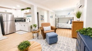 A compact living space with a kitchenette, a sofa, a small round table with a plant, a bunk bed, and a dresser. - ☀️Newly renovated cottage at the coast….60 second walk to the beach🌊 (North Topsail Beach)